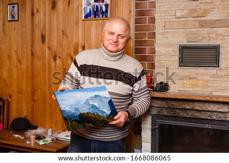elderly man holding a photo canvas in a wooden house