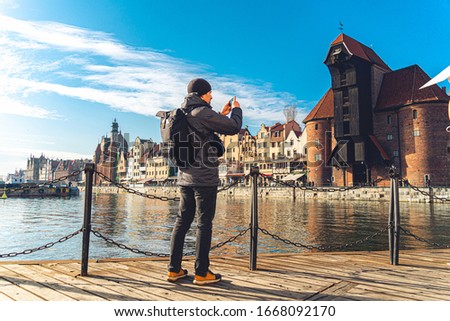 Theme of tourism in Poland. Traveling in Gdansk. A male traveler uses a phone on the embankment of the Motlawa River amid the main attraction, a symbol of the city of Gdansk Gate crane or Brama zuraw