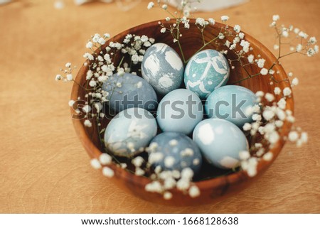 Modern Easter eggs in wooden bowl with spring flowers  on rustic table. Stylish pastel blue Easter eggs painted in natural dye from red cabbage. Happy Easter. Rural still life