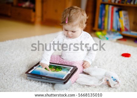 Cute adorable baby girl watching cartoons on tablet pc. Todder child at home touching on screen and playing educational games on computer.