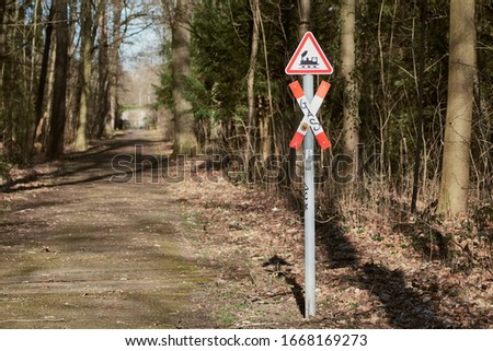 Country lane in the forest and a red and white train crossing sign. Railroad crossing warning and crossbuck in a rural area in Karlsruhe, Germany