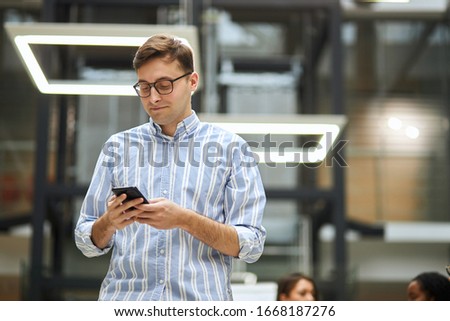 young clever man in glasses working with cell phone. low angle view . gadget, guy briwsing the net, download files, documents, photos, music, looking for wi-fi connection.blurred background