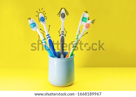 Colorful toothbrushes in the form of cartoon characters in a blue glass on a yellow background. The concept of family hygiene.