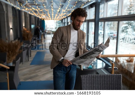 handsome bearded businessman in fashion beige jacket and jeans standing and reading newspaper, close up photo. free time, spare time,lifestyle