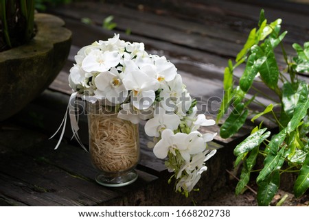 Gorgeous bridal wedding bouquet of white roses, hydrangeas, ozotamnusa,eucalyptus and orchid in glass vase on beautiful concrete path with green left background