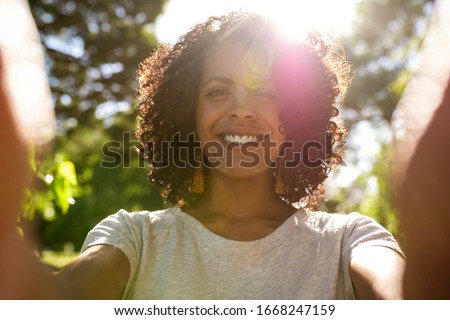 Smiling young woman taking a selfie while enjoying a sunny summer afternoon outside in a park