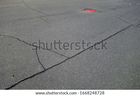 Craked asphalt and red manhole cover. Industrial background and texture for design.