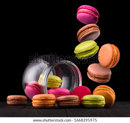 Flying french colorful macaroons and jar on wooden table isolated on black background with clipping path