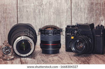 Old film camera, digital lenses and pocket mechanical watch on a light wooden background