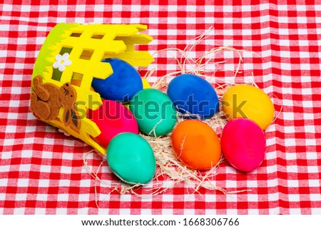 Happy Easter greeting card template. A overturned basket with colorful easter eggs with straw on a red checkered tablecloth.  Beautiful card backdrop. Religion and culture concept.