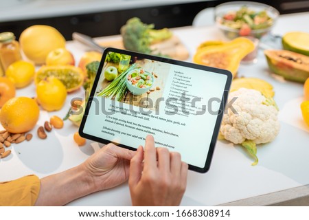 Woman looking on the digital recipe, using touchscreen tablet while cooking healthy meal on the kitchen at home, close-up view on the screen Royalty-Free Stock Photo #1668308914
