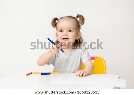 child a girl two years old sits at a table and draws on a white background
