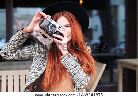 Outdoor spring lifestyle portrait of pretty young woman having fun in caffe. Photographer making pictures in hipster style clothes and hat. 