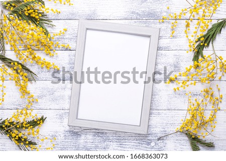 Easter decor with mimosa flowers and frame on wooden table. Mockup with a gray frame. Top view. Copy space - Image
