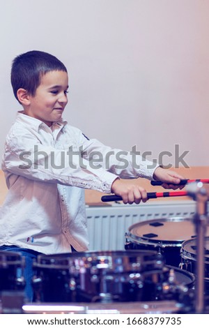 Boy drumming. boy in a white shirt plays the drums. vertical photo. toned.