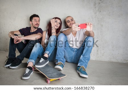 Skateboarder friends taking photo portrait with mobile phone against concrete wall.