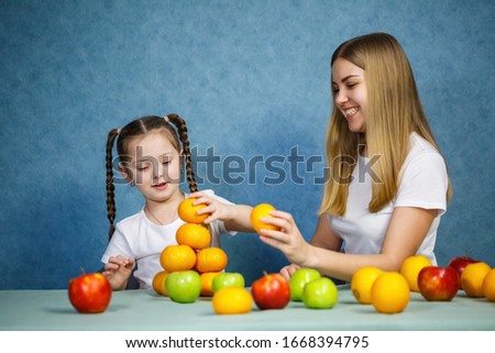 Little girl and mom play with fruits and fool around. They are wearing t-shirts