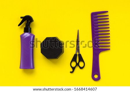 Beauty topic: stylist scissors, hairspray, hair wax, and stylist's comb over yellow background. Fashion and style concept.