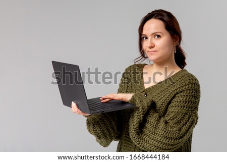 Charming young woman working freelance, remote from office, hold laptop, typing university essay, turn left smiling copy space, stand gray background joyful, browsing web using computer