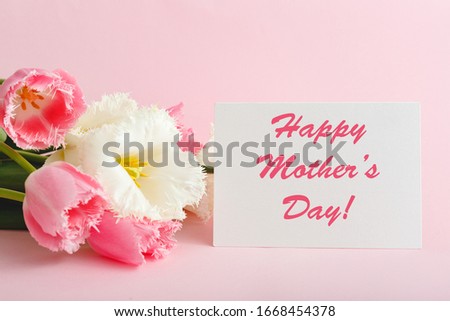 Happy Mothers Day text on gift card in flower bouquet on pink background. Greeting card for Mom. Flower delivery, Congratulations card in flowers for women. Greeting card in pink tulips.