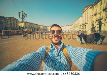 happy man tourist visiting the city centre of Turin and taking selfie with smartphone. Piedmont region, Italy. Vintage color post production