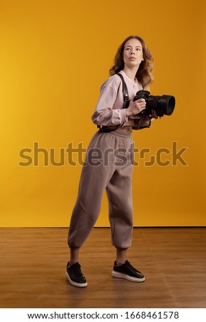 Young girl freelancer photographer posing with photo camera in hands on a yellow background