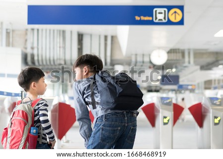 Asian big brother student teach and comfort his young brother boy to take train at city platform to school on their own together. Independence, self confidence, child development, brotherhood concept