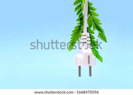 Electric white plug with green leaves hanging  and isolated on blue background. Eco friendly, alternative ecological energy,  ecology concept. Copy space. 