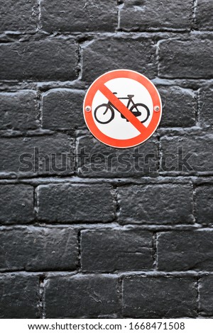 Vertical, full-frame, black brick worn texture wall surface with no bicycle parking sign, photographed in daylight in Amsterdam city. Do not park your bike here warning to cyclists posted publicly