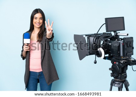 Reporter woman holding a microphone and reporting news isolated on blue background happy and counting three with fingers