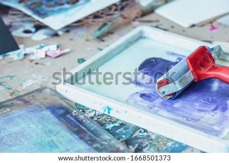 Red ink roller and splashed blue paint in tray - creative printmaking tools