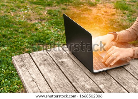 Human Female Hands working on PC grey Laptop on wood table in green park background with sunlight effect. Freelance worker. Productivity, planning concept. Active lifestyle. Smart working