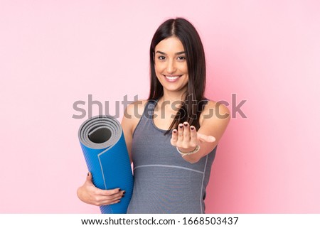 Young caucasian woman with mat isolated on pink background inviting to come
