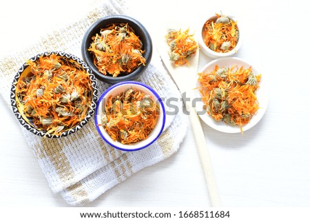 Petals of chopped dried calendula, displayed in containers on white wooden background