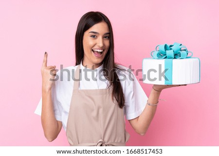 Young woman with a big cake over isolated background pointing up a great idea