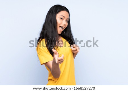 Teenager Chinese woman isolated on blue background pointing to the front and smiling