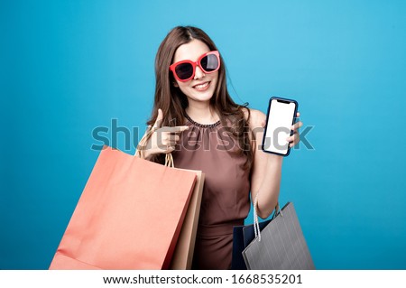 Beautiful mix race caucasian asian woman are holding shopping bags and smartphone with face happily in blue seamless,isolated background. Shopping lifestyle, online shopping concept.
 Royalty-Free Stock Photo #1668535201