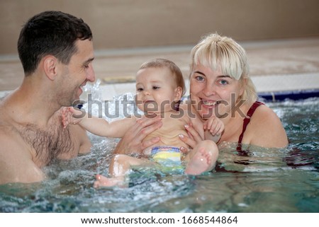 Small baby girl is swimming in the pool. Dad and mom bathe a little girl in the pool,
