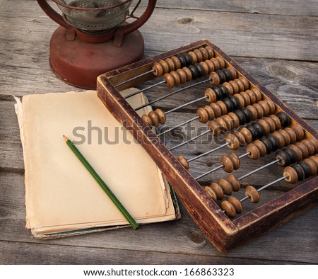 Old abacus, the paper with a pencil next to a kerosene lamp on a wooden table Royalty-Free Stock Photo #166863323