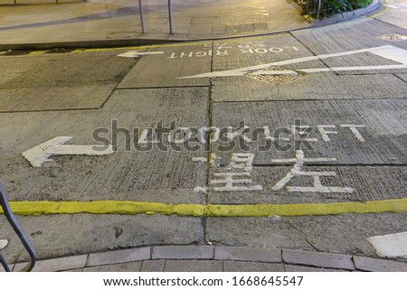 Pedestrian crossing with caution marking "Look left" painted on the road at Hong Kong city, China. The inscription is made in English and Chinese. Low light at night, selective focus