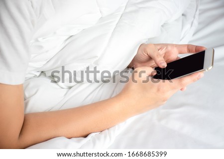 Close up of an Asian hand using a smartphone on the bed in the room.