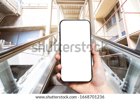 Close-up of female use Hand holding smartphone with empty blank white screen blurred images touch of Abstract blur of mechanical escalator for people going up and down, modern escalators in mall