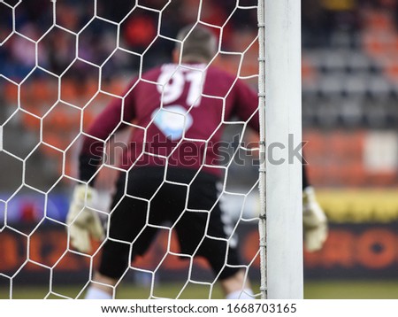 Detail of goal's post with net and football goalkeeper in the background.