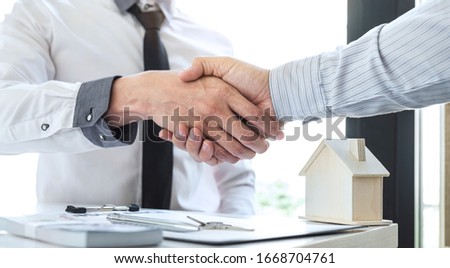 Real estate agent are shaking hands after good deal and giving house, keys to customer after signing contract to buy house with approved property application form.