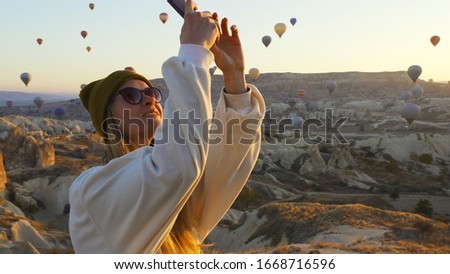 Young female taking pictures of air balloons by smart phone