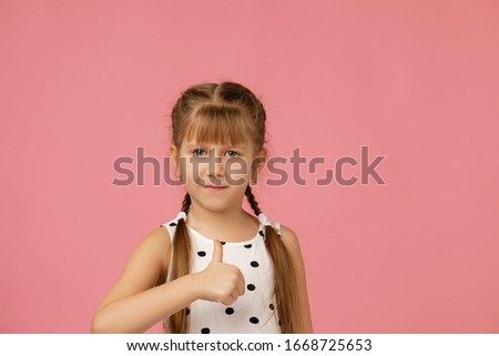 happy beautiful little child girl in dress showing thumbs up on pink background.