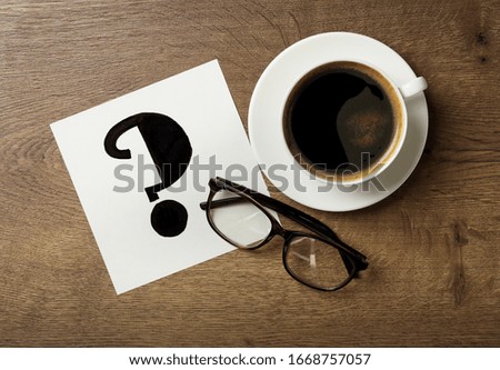 Note with question mark, eyeglasses and cup of coffee on wooden table, flat lay