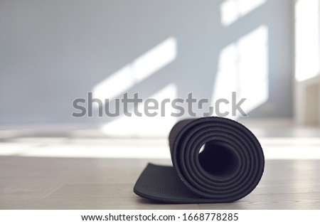 Black yoga mat on the floor of a bright sunny studio. Royalty-Free Stock Photo #1668778285
