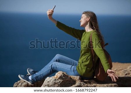 Happy girl traveler with a backpack takes a selfie on a smartphone on the background of the sea and smiles. The concept of travel. Copy space.