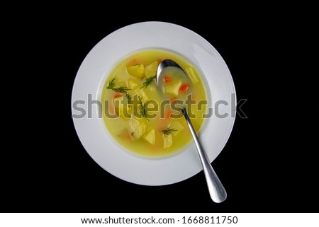 White milk soup with potatoes, carrots, greens stands in a white plate isolated on black background.